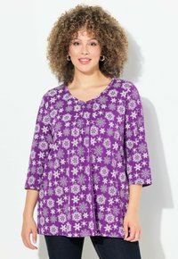 Tunic floreale viola con scollo a V, caratterizzata da maniche a tre quarti e una vestibilità ampia, decorata con intricati motivi floreali bianchi.