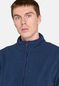 Marine fleece jack met hoge kraag, ritssluiting en een gladde textuur. Beschikt over een ritszak en een minimalistisch ontwerp.