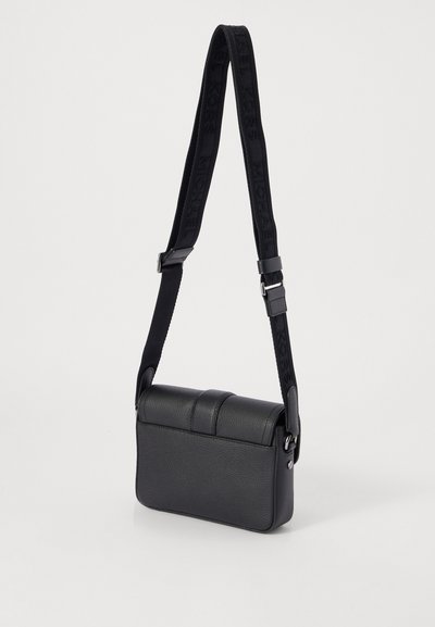 Sac bandoulière noir en cuir texturé, de forme rectangulaire, avec un haut rembourré et une sangle réglable arborant un logo embossé.