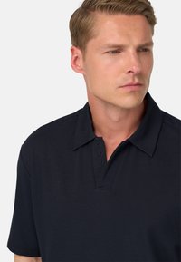 Polo de color navy hecho de una tela suave, con un cuello tradicional que presenta detalles de marca en la parte del cuello, mangas cortas y un corte clásico.