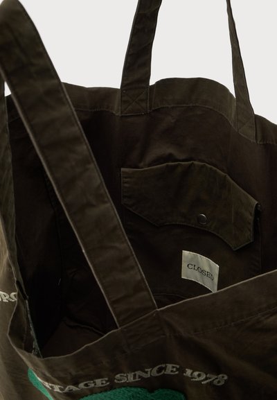 Sac cabas en tissu marron foncé avec deux anses, une poche intérieure avec un bouton-pression et une étiquette portant la mention "CLOSED" à l'intérieur de la poche.