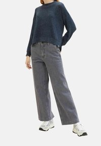 Sininen teksturoitu ylisuuri neule yhdistettynä harmaisiin leveälahkeisiin farkkuihin ja valkoisiin urheilukenkiin, rento istuvuus ja yksinkertainen muotoilu.