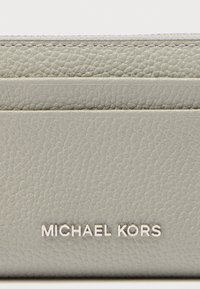 Portefeuille en cuir gris texturé avec une finition lisse, arborant un logo "MICHAEL KORS" en relief avec une garniture en métal argenté en bas.