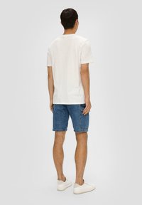 Witte t-shirt met korte mouwen gecombineerd met blauwe denim shorts en witte sneakers. De stof lijkt soepel, en het ontwerp is eenvoudig en casual.