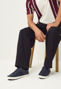 Mørkeblå sneakers med hvid sål, med røde og blå striber. Bruges med sorte bukser og en stribet bordeaux og hvid skjorte.