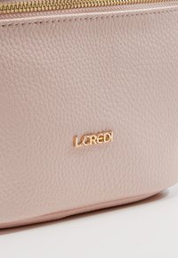 Pochette en cuir rose clair texturé avec fermeture éclair dorée et petit logo métallique doré portant l'inscription L.Credi au centre avant.