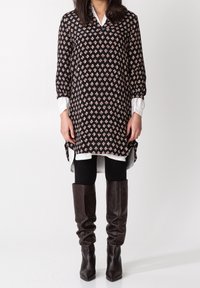 Czarna tunika w wzory z kwiatowymi motywami, w połączeniu z białą koszulą, czarnymi legginsami i brązowymi skórzanymi botkami do kolan.