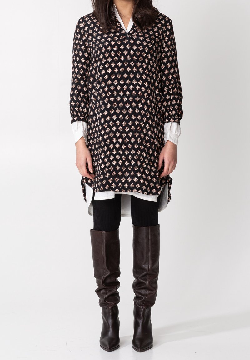 Czarna tunika w wzory z kwiatowymi motywami, w połączeniu z białą koszulą, czarnymi legginsami i brązowymi skórzanymi botkami do kolan.