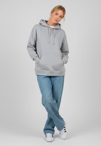 Felpa grigia con una comoda tasca a marsupio, stringhe e polsini a coste, abbinata a jeans azzurri e sneakers bianche.