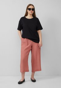 Czarny bawełniany t-shirt, luźny krój; teksturowane różowe spodnie typu cropped; czarne siateczkowe buty na wsuwkę; oversize'owe czarne okulary przeciwsłoneczne.