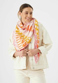 Écharpe carrée multicolore avec des motifs géométriques audacieux en rose, orange et jaune, fabriquée en tissu doux et texturé, portée de manière décontractée.