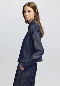 Veste bleu marine texturée avec un col et des poignets boutonnés. Présente un design court avec des rayures verticales et une coupe décontractée.