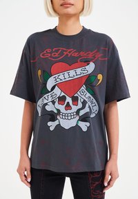 Černé grafikové tričko s potiskem lebky, červeného srdce a bannerem s nápisem "LÁSKA ZABILY POMALU." Krátké rukávy, volný střih a jemný bavlněný materiál.