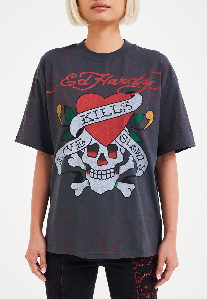 Černé grafikové tričko s potiskem lebky, červeného srdce a bannerem s nápisem "LÁSKA ZABILY POMALU." Krátké ruk�ávy, volný střih a jemný bavlněný materiál.