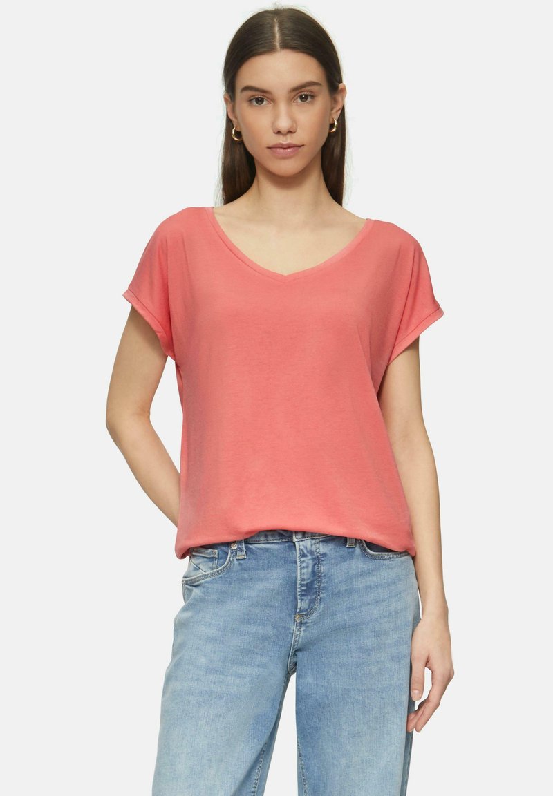 Korallefarbenes V-Ausschnitt-T-Shirt mit kurzen, hochgerollten Ärmeln, aus weichem Stoff. Kombiniert mit hellblauen Denim-Jeans und einem lockeren Schnitt.