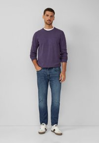 Lila Langarmshirt über einem weißen Rundhalsausschnitt, kombiniert mit blauen Jeans und weißen Sneakern, die graue und schwarze Akzente aufweisen.