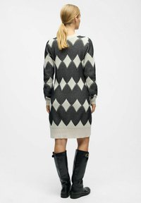 Robe en tricot crème et noire avec un motif géométrique en losanges, présentant des manches longues et un ourlet côtelé, associée à des bottes noires montantes.