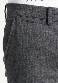 Grijze herringbone stofbroek met een platte voorkant, zijzakken en een soepele tailleband, met een subtiele textuur en een getailleerde pasvorm.