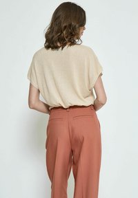 Beige lyhythihainen paita, jossa on rento malli, yhdistettynä korkeavyötäröisiin rautanruskeisiin housuihin, joissa on sileä pinta ja takataskut.