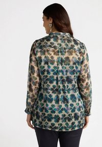 Przezroczysta bluzka w wielokolorowy kwiatowy wzór w odcieniach zieleni, niebieskiego i purpury. Posiada spiczasty kołnierzyk oraz rękawy z guzikami.