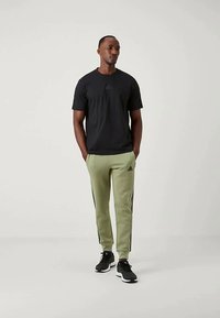 Μαύρη κοντομάνικη μπλούζα συνδυασμένη με ανοιχτό πράσινο παντελόνι φόρμας με μαύρες ρίγες στο πλάι, φορεμένα με μαύρα αθλητικά παπούτσια.