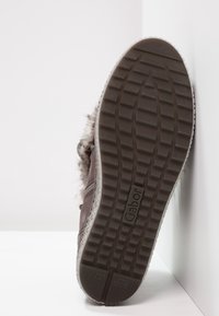 Scarpa in suede marrone con suola in gomma texturizzata, dotata di dettagli in pelliccia sintetica e una zip laterale per una facile calzata. Logo del marchio visibile sulla suola.