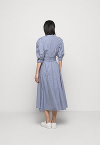 Blå och vit rutig klänning med puffärmar, en åtsittande midja och en flödande kjol. Buren med vita sneakers, visad från baksidan.