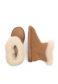 Tan suede ankle boots with a fluffy cream sheepskin collar, rounded toe, flat rubber sole, and visible stitching accents.