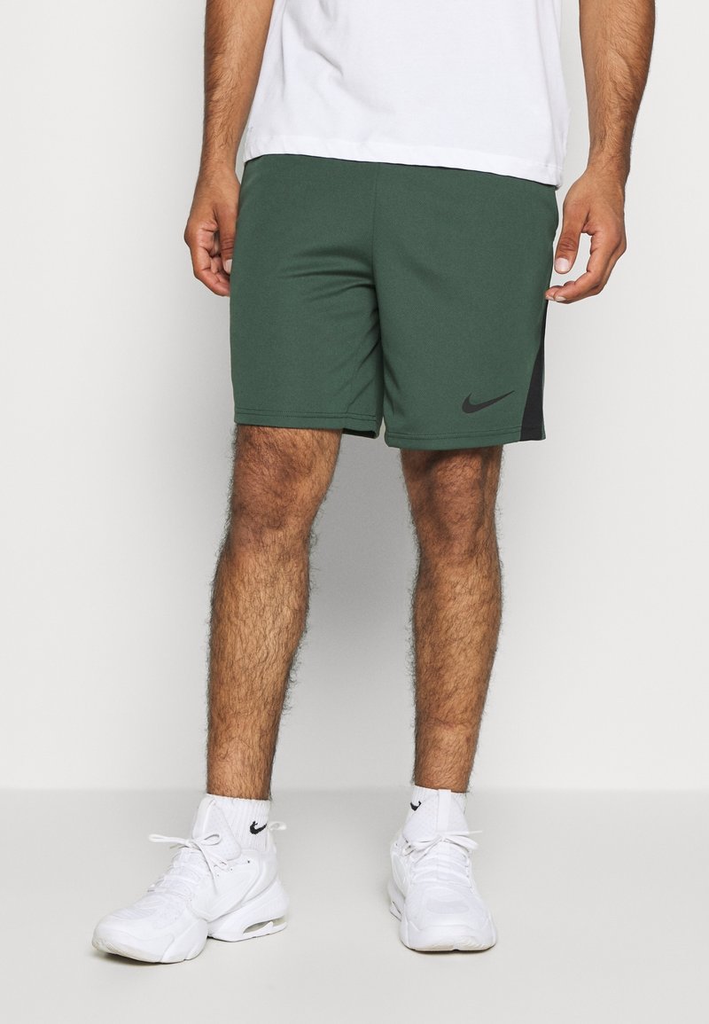 Shorts de sport Nike verts avec un panneau latéral noir, fabriqués en tissu lisse. Dotés d'une taille élastique et d'un petit logo sur la cuisse gauche.