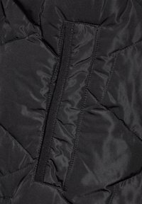 Svart quiltad tyg med en slät struktur, synliga sömnadsmönster och en dold dragkedjedetalj.