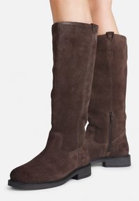 Bottes en daim marron à hauteur de genou avec une semelle en caoutchouc noir plat, fermeture éclair sur le côté et détails de couture le long des coutures. Texture lisse avec des accents minimaux.