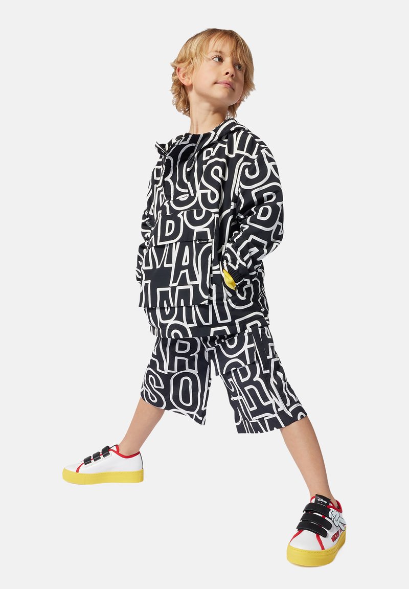 Zwart-witte jas en korte broek met letterpatroon, gecombineerd met witte sneakers met rode en gele accenten.