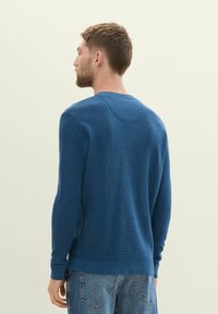 Sudadera de punto azul con un acabado texturizado, mangas largas y un escote redondo, combinada con jeans de mezclilla azul claro.