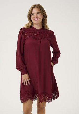 Vestido burdeos con mangas largas, botones en el frente y encaje en el cuello y el dobladillo. Hecho de una tela suave con un corte holgado.