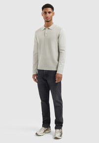 Helle graue Langarm-Polohemd mit strukturiertem Strick, ausgestattet mit einem Kragen und einer Drei-Knopf-Leiste, kombiniert mit dunklen Slim-Fit-Jeans und Turnschuhen.