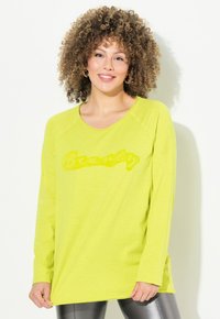 Maglietta a manica lunga verde lime con una grafica testurizzata "Beauty" in una tonalità leggermente più scura, con vestibilità rilassata e spacchi laterali.