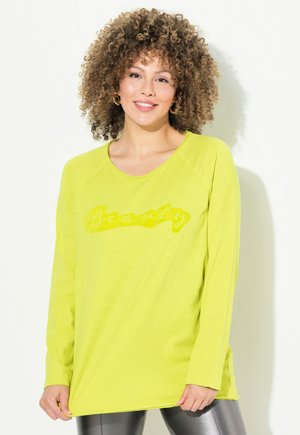 Maglietta a manica lunga verde lime con una grafica testurizzata "Beauty" in una tonalità leggermente più scura, con vestibilità rilassata e spacchi laterali.