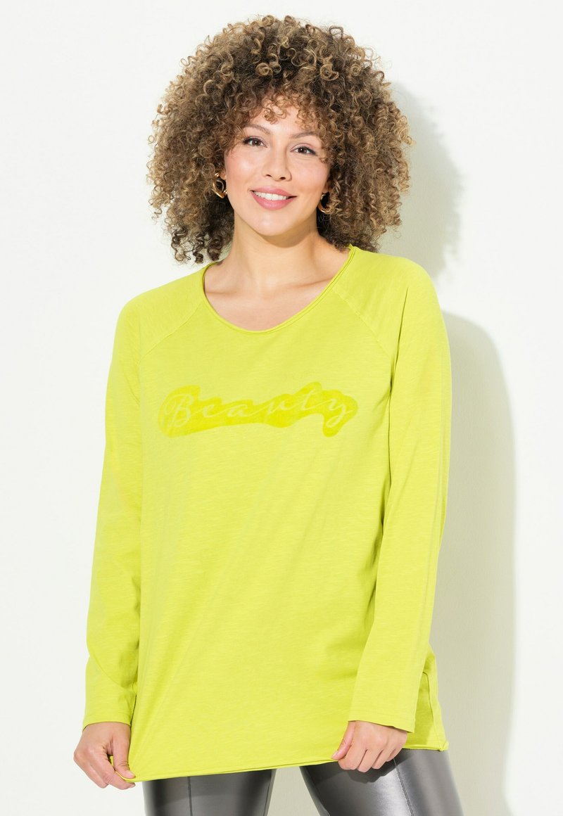 Maglietta a manica lunga verde lime con una grafica testurizzata "Beauty" in una tonalità leggermente più scura, con vestibilità rilassata e spacchi laterali.