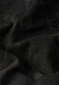 Czarna tkanina o gładkiej teksturze i delikatnym połysku, z drobnymi, poziomymi liniami i lekkim marszczeniem, co wskazuje na miękki opad.