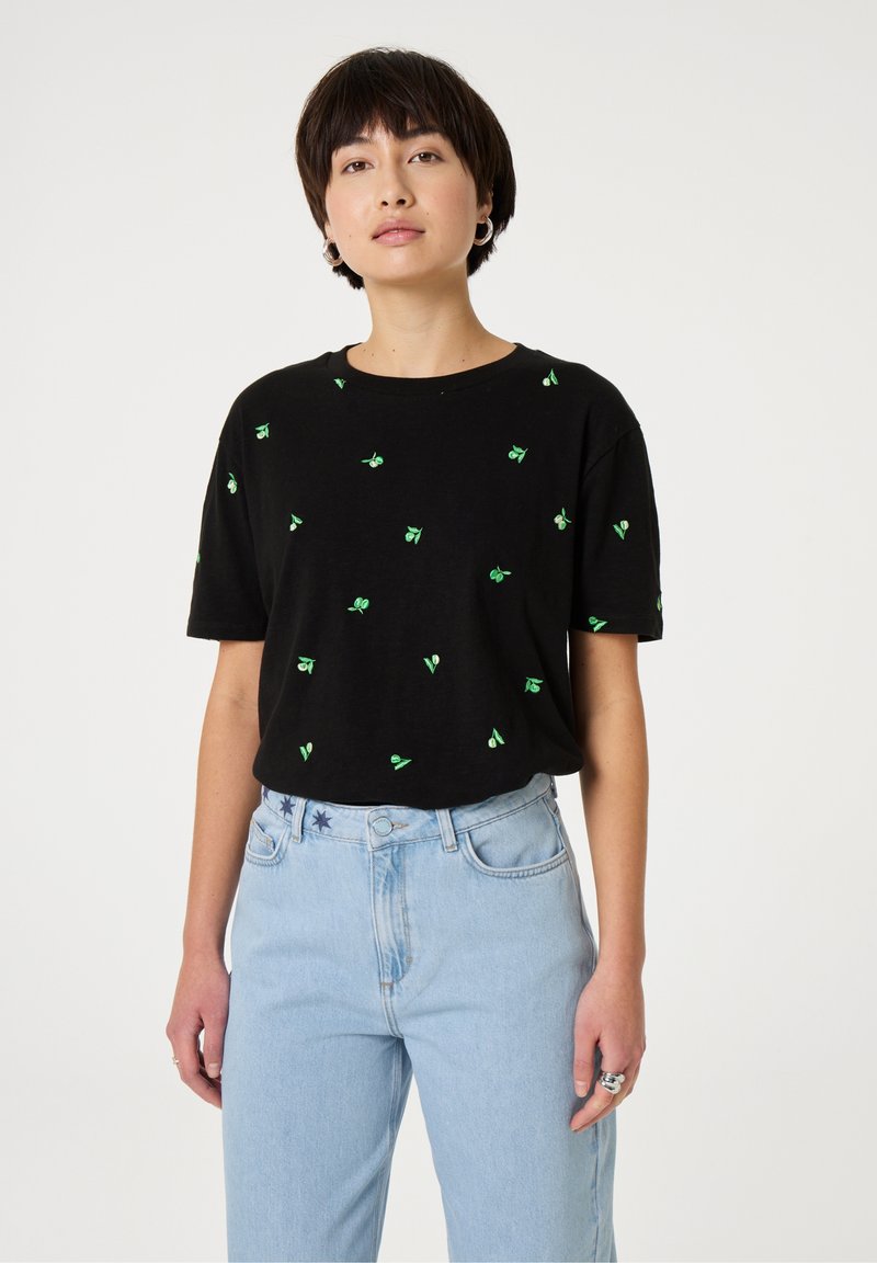 Zwart katoenen T-shirt met korte mouwen, versierd met verspreide groene bladvormige borduursels. Gecombineerd met lichtblauwe high-waisted jeans.