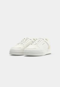 Pair of white low-top sneakers with laces, minimal perforated details, and a subtle brand logo on the side, shown on a plain background.