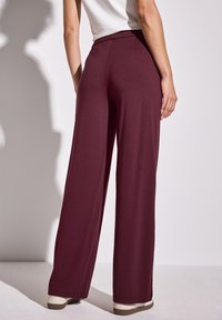 Pantalons larges bordeaux en tissu doux, avec une taille lisse et une coupe décontractée, légèrement extensibles et sans motifs visibles.