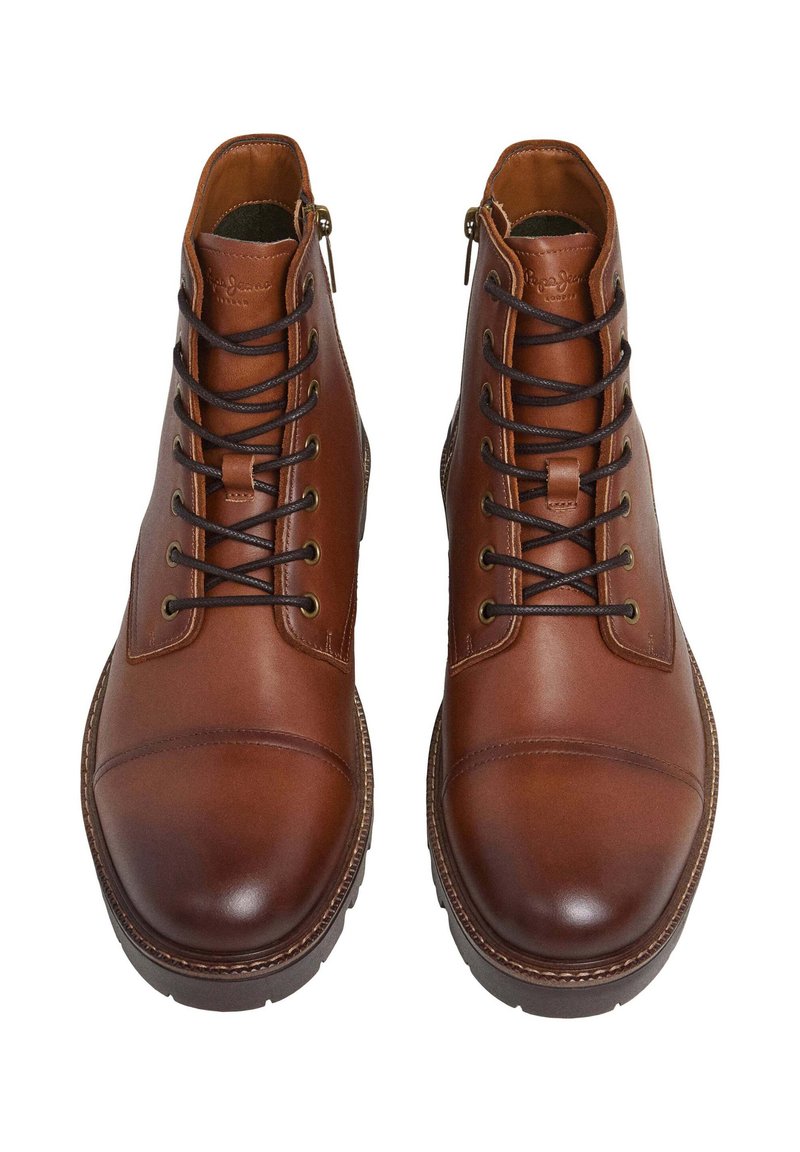 Botas de piel marrón hasta los tobillos con punteras redondeadas, que presentan cordones negros, ojetes dorados, cremalleras laterales y detalles de costura a lo largo de la suela.