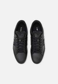 Musta nauhalenkki kenkiä, joissa on tekstuurilla varustetut varvastopit ja sivulogot, nähtynä ylhäältä valkoisella taustalla.