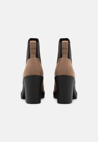 Botines de ante marrón con paneles elásticos negros a los lados y un tacón grueso y sólido de color negro. Textura suave con punta redondeada y detalles mínimos.