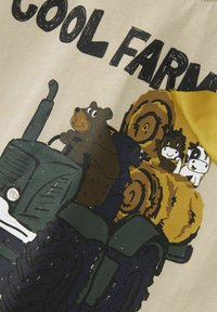 Diseño de tractor verde con un oso marrón y dos animales de dibujos animados sobre pacas de heno. El fondo presenta una tela color crema con el texto "FARM COOL".