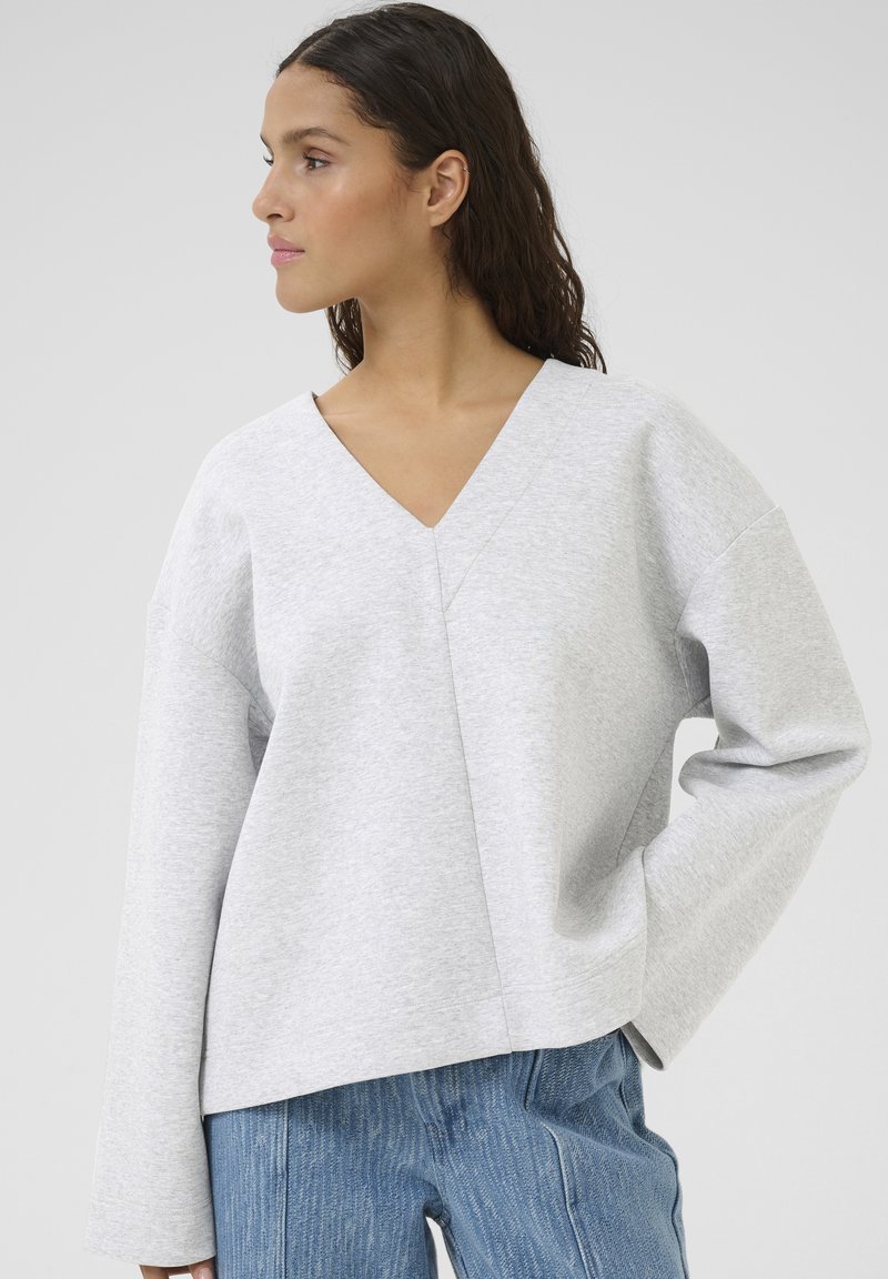 Grå sweater med V-hals, løstsiddende design og lange ærmer. Stoffet ser blødt ud, som om det er lavet af fleece eller sweatshirt-materiale.