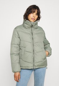 Vadderad jacka i ljusgrön, med hög krage, dragkedjeslutning och horisontell sömnad. Inkluderar framfickor och en smidig textur.
