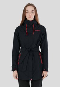 Giacca nera impermeabile con vita cinchata, accenti rossi, cappuccio e tasche con zip. Realizzata in tessuto liscio e resistente alle intemperie.