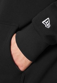 Sudadera negra con capucha que cuenta con un bolsillo lateral y puños de canalé. Logo notable en blanco en la manga. Tejido suave con una textura lisa.